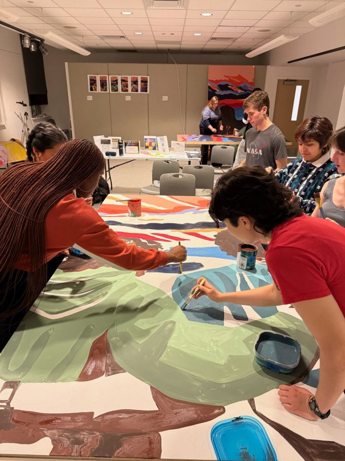 Students work on the 2025 Mending Walls Penn State mural during an evening Painting & Talking session.