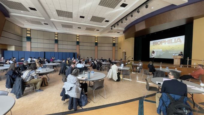 A conference room with people sitting at circular tables facing a stage with a podium.