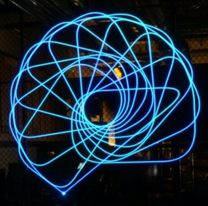 Long exposure photo showing a complex, blue, spiral-patterned light drawing using a 6-axis robot arm; coding and design by Vernelle Noelle
