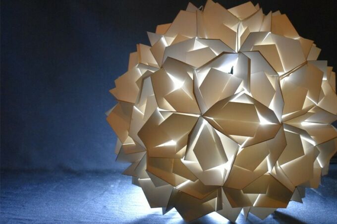 A spherical architectural lantern with light emanating from within a repeating pattern of laser-cut facets.