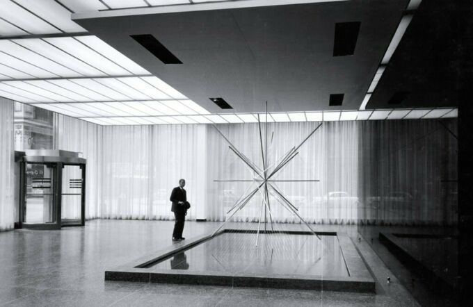A black and white photograph of a man observing an art sculpture in the Inland Steel Building in Chicago (1958).