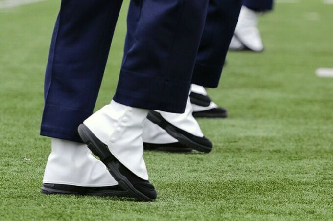 A close up of a row of white spatted band shoes as the blue band marches and performs during a halftime performance.