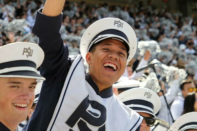 During college game day, a blue band member cheers in the stands during the football game.
