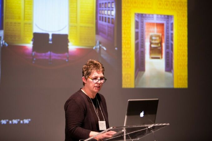Penn State art professor Cristin Millet presenting in front of brightly colored screen.