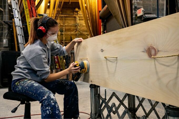 A student sanding the surface of a large piece of wood.