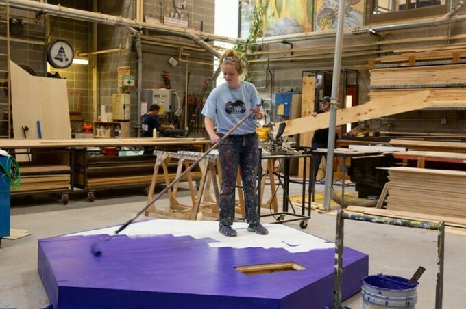 A student painting multiple platforms to be used as props in a School of Theatre production.