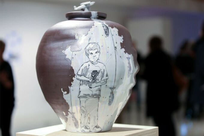 A smooth ceramic vase showcasing a section of it etched away with a detailed illustration of a young boy catching fish.