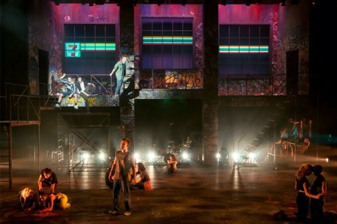 A scene from the production of American Idiot, showcasing a musical number with the ensemble cast singing and dancing on stage and in the rafters.