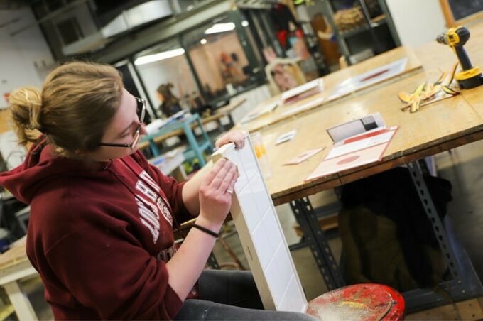 SoVA student sanding a wooden frame edge of a white-tiled sculpture base.