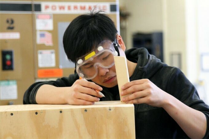SoVA student centering and measuring a piece of wood to attach to a wooden box.
