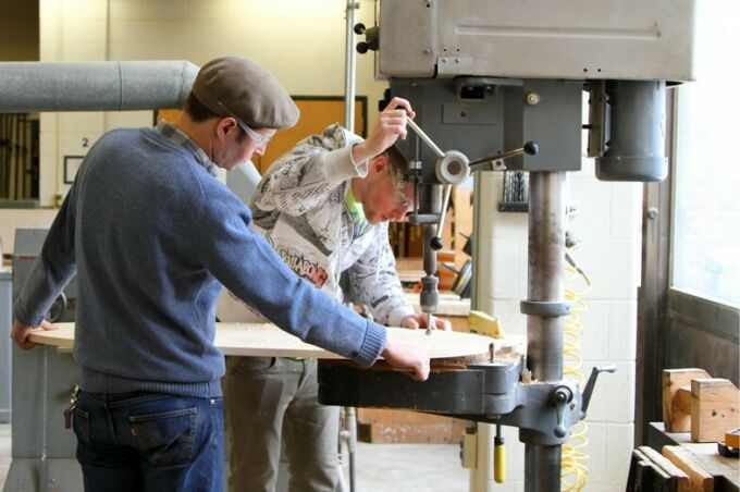 A SoVA student aligning a piece of equipment before he drills a hole through a circular piece of wood.