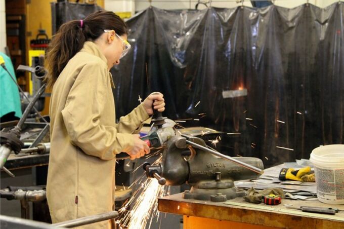 SoVA student using a hand-held cutting saw to cut and smooth a piece of metal tube.