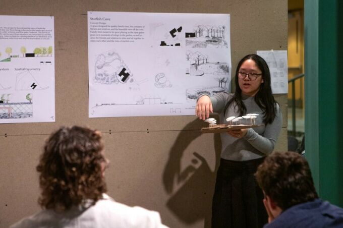 A landscape architecture student explains her project while holding a model during a critique.