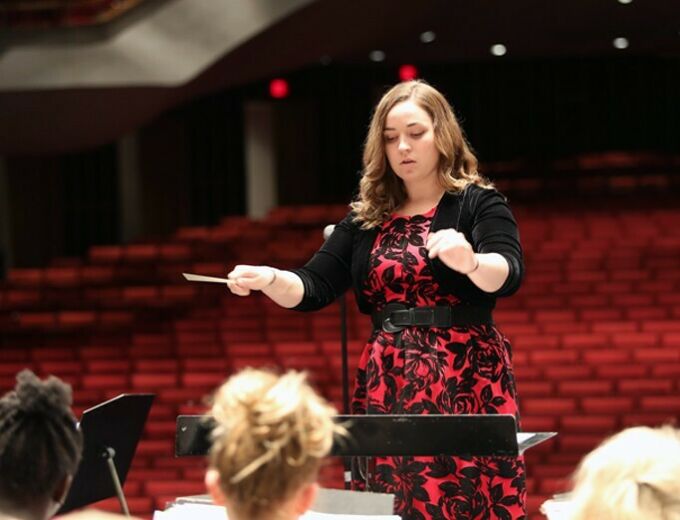Conductor in red and black dress faces musicians in Eisenhower auditorium