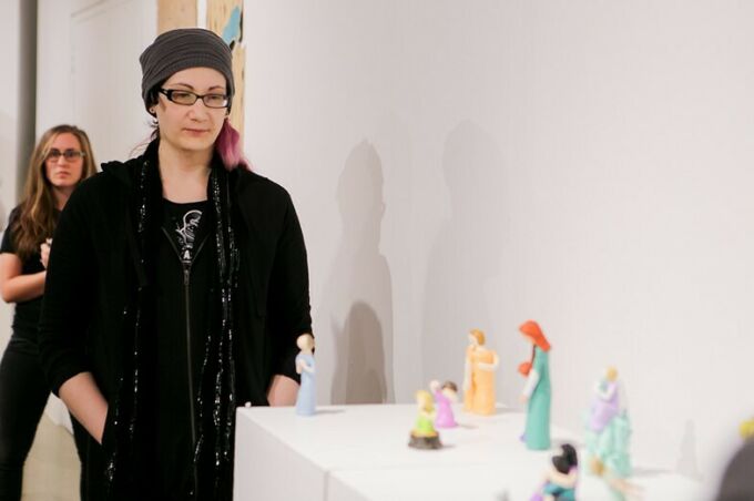 A student examines brightly colored figurines of women and children displayed in Zoller Gallery during the first year MFA student exhibition.