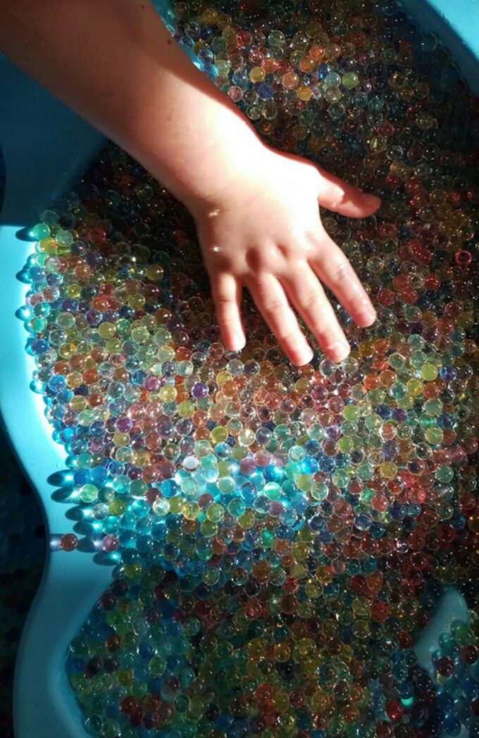 A photograph of a child's hand interacting in a tub of colorful water beads.
