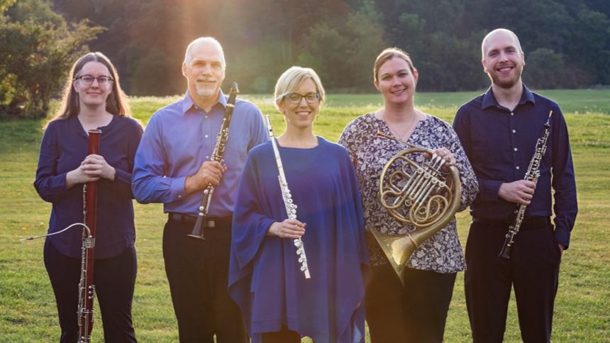 Five Penn State Music faculty members who make up the Pennsylvania Quintet, posing in a green, grassy field with trees and sun flare in the background.