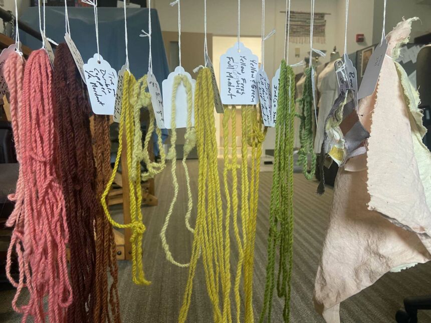 Strands of died yarn in red, yellow, and green hang from white strings.