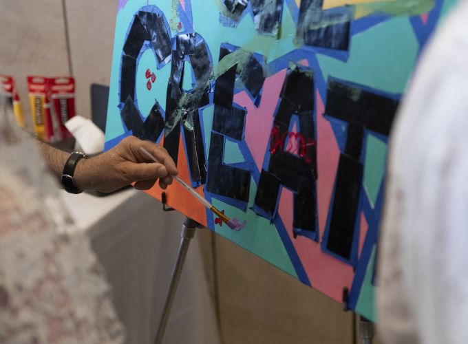 A donor paints a small design on the "We Create" canvas.