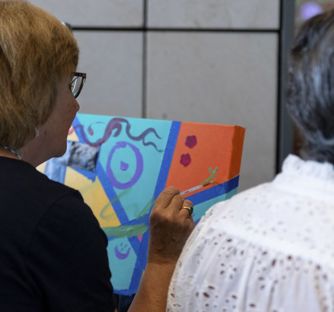 A donor paints a small design on the "We Create" canvas.