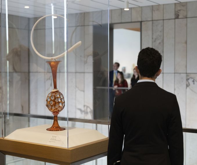 Back view of a man standing next to a sculpture on display.