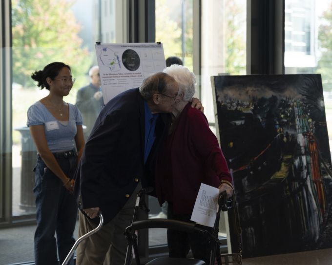 Two elderly donor attendees hugging each other while a student smiles at them.