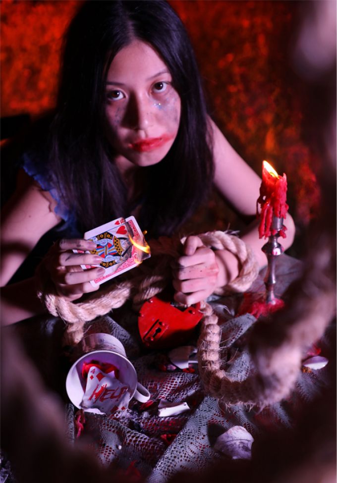 A poster featuring of a dark-haired woman with smeared red makeup holding a deck of playing cards in one hand and a rope in the other.