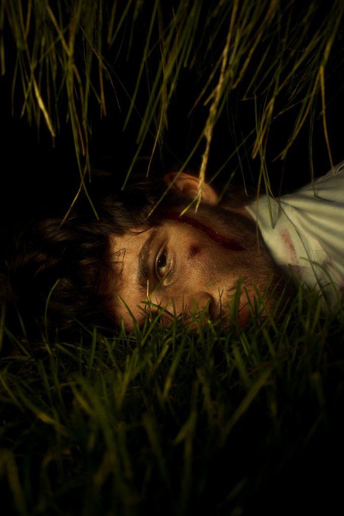 A photograph of the head and neck of a man lying in tall grass at night.
