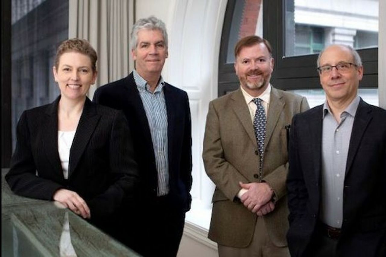 Three men and a woman in business attire smile at the camera.