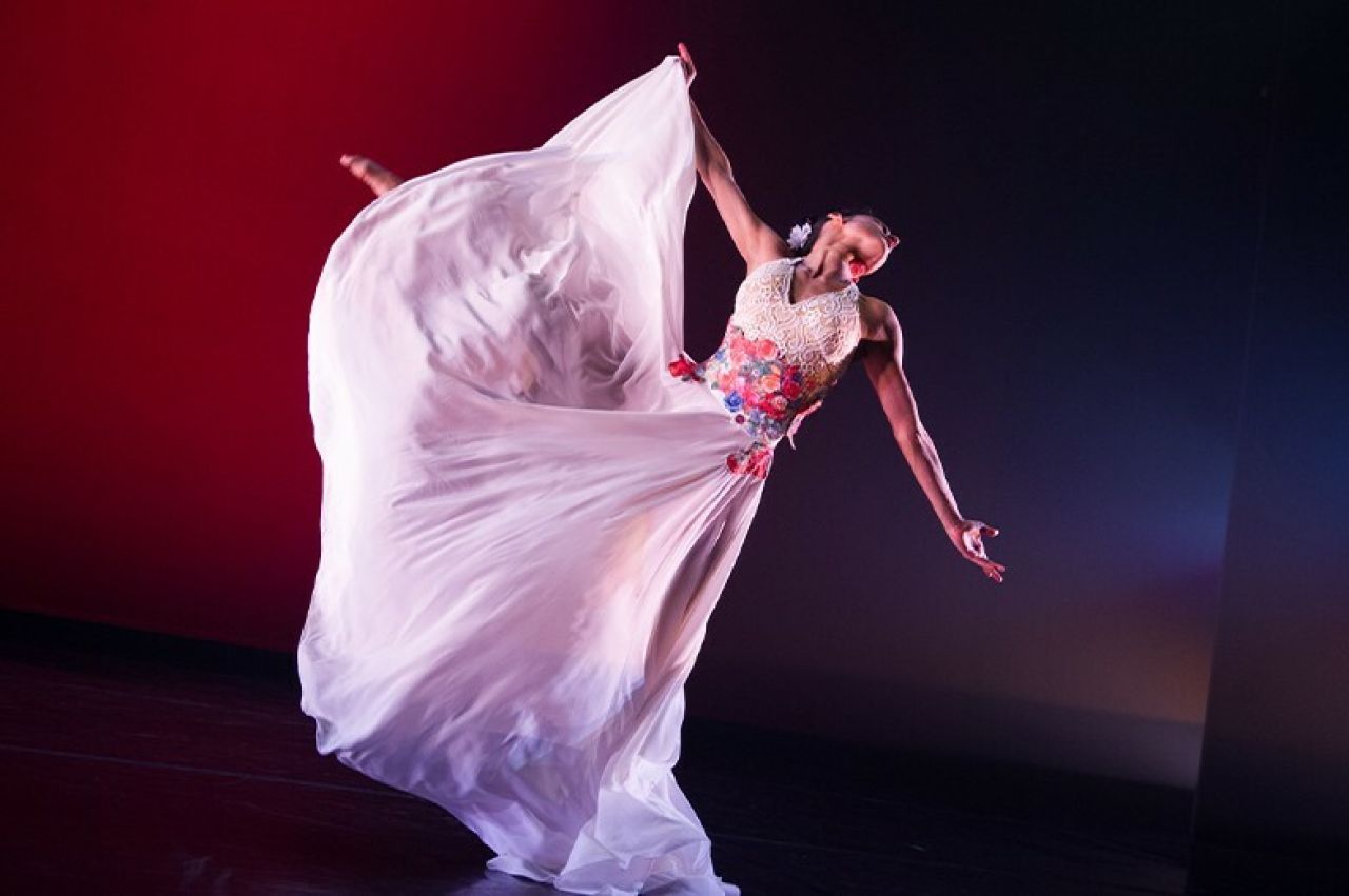 A woman wearing a flowing gown outstretches her arms.