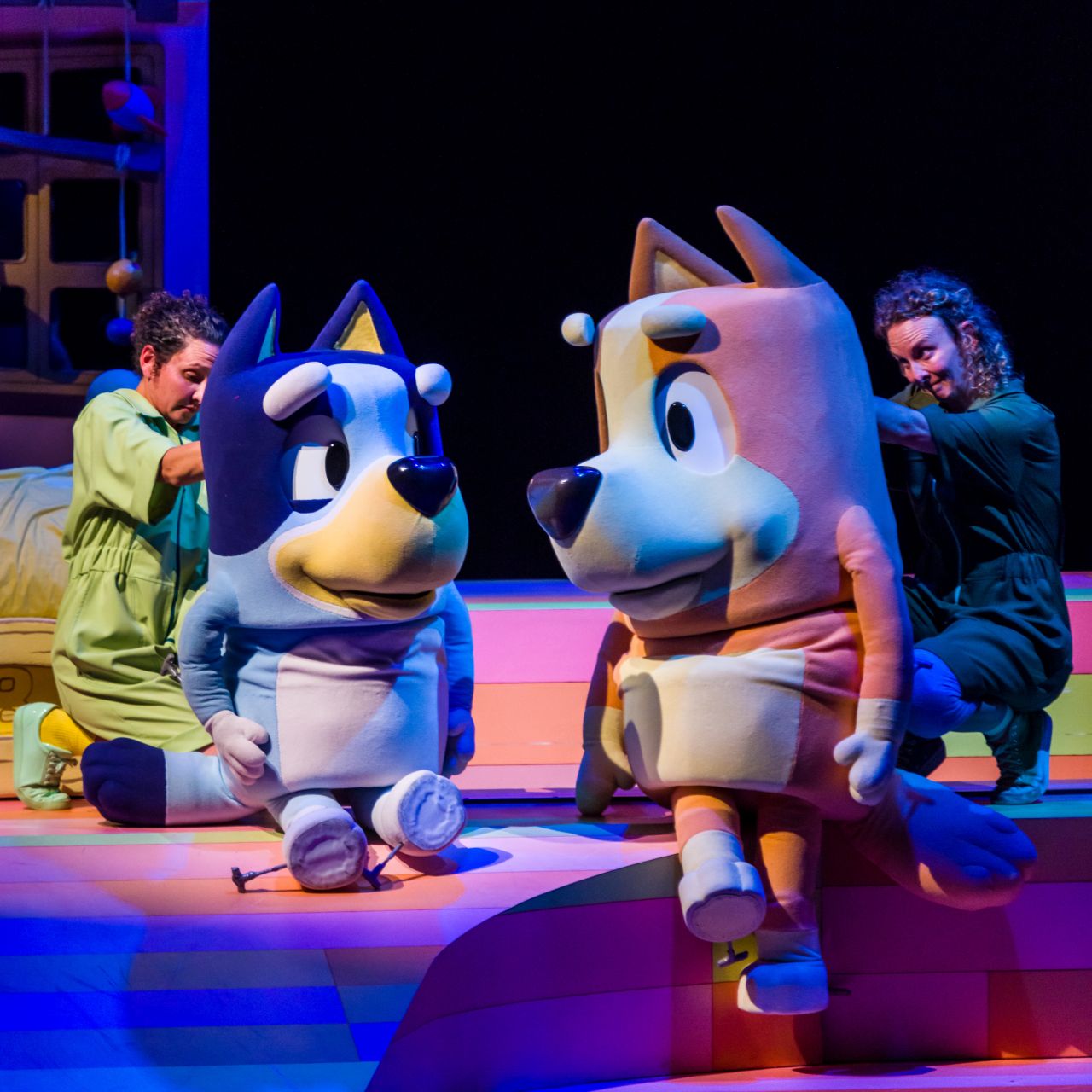 Actors stand behind two oversized cartoonish dog puppets.
