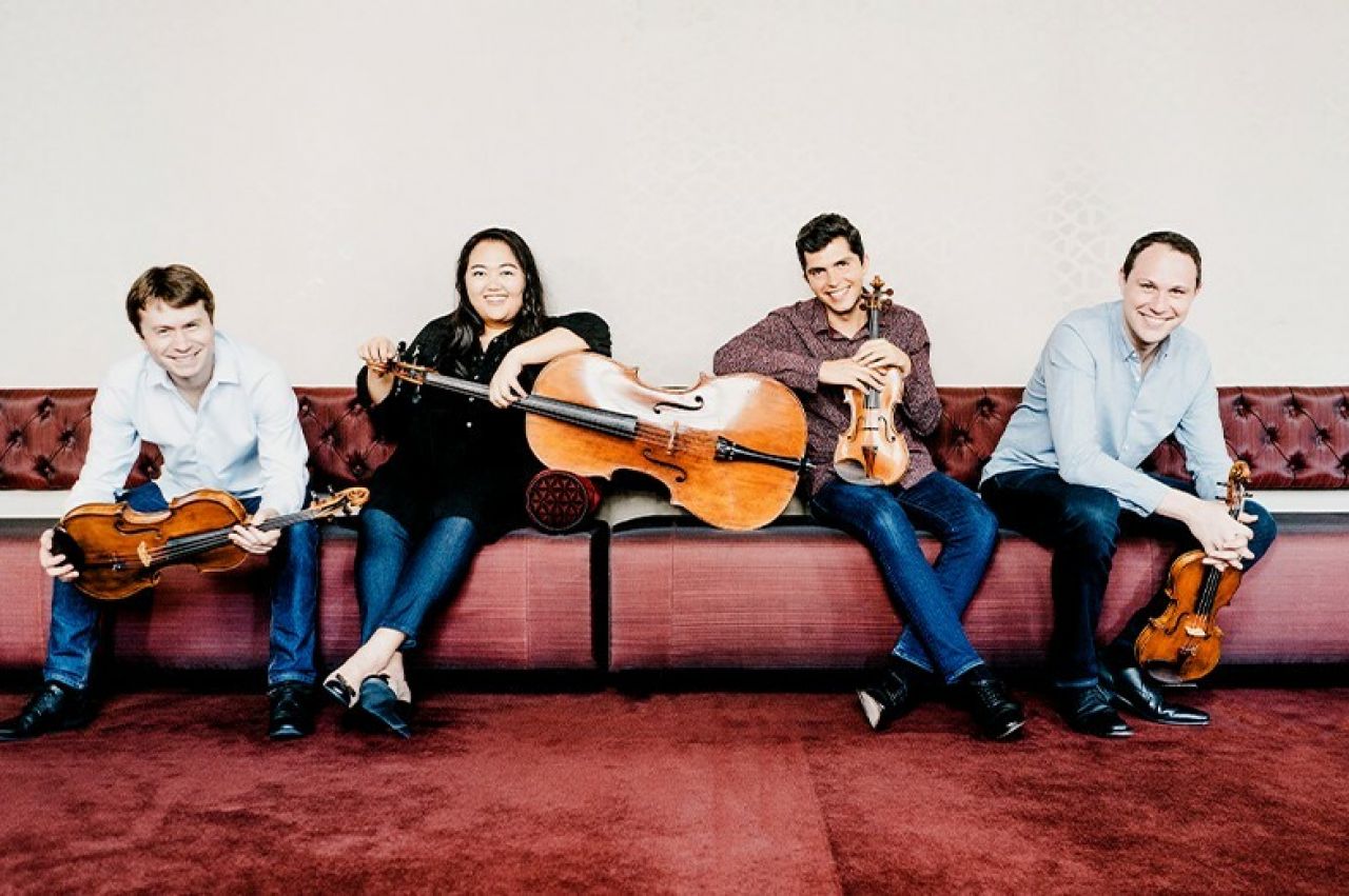 Four musicians sit on a couch and hold their classical instruments.