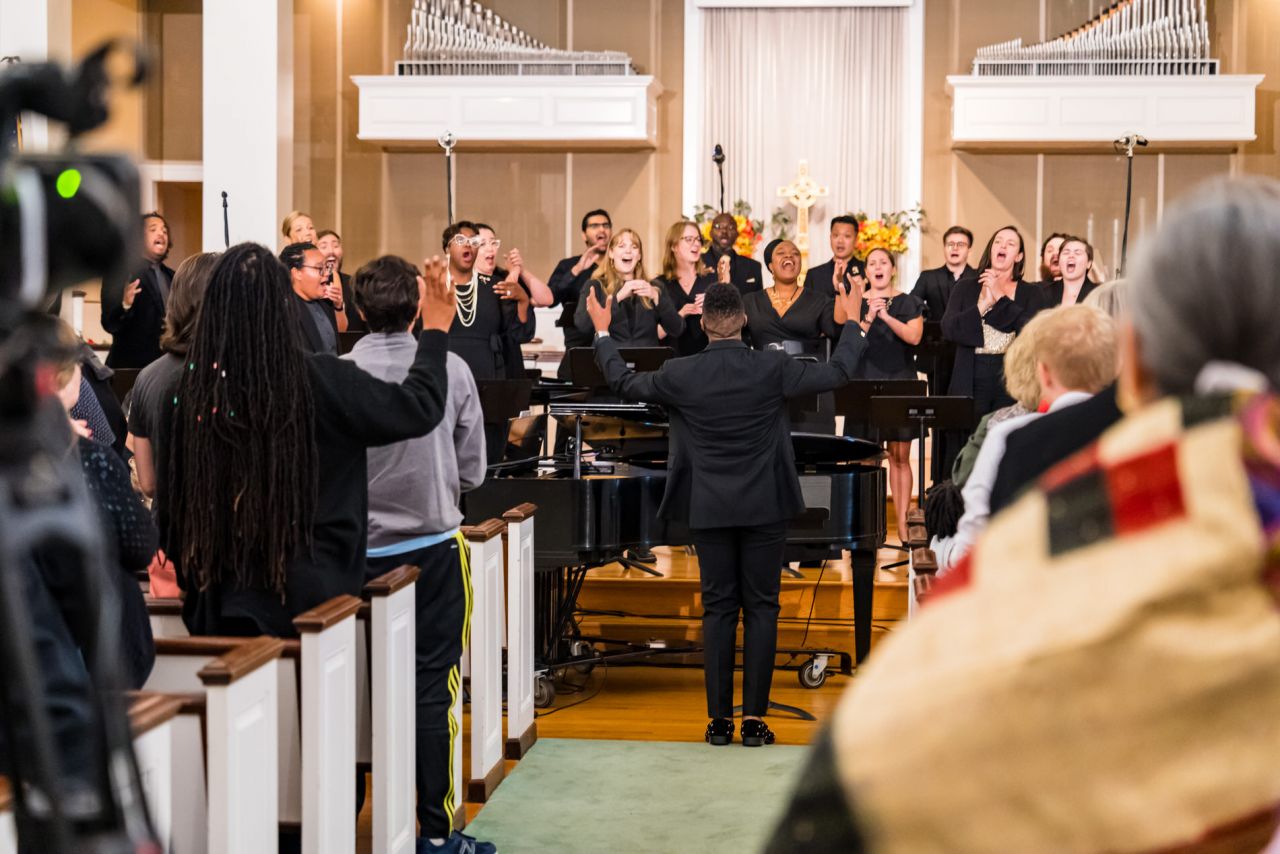 A diverse choir performs at the front of a church in front of a congregation.