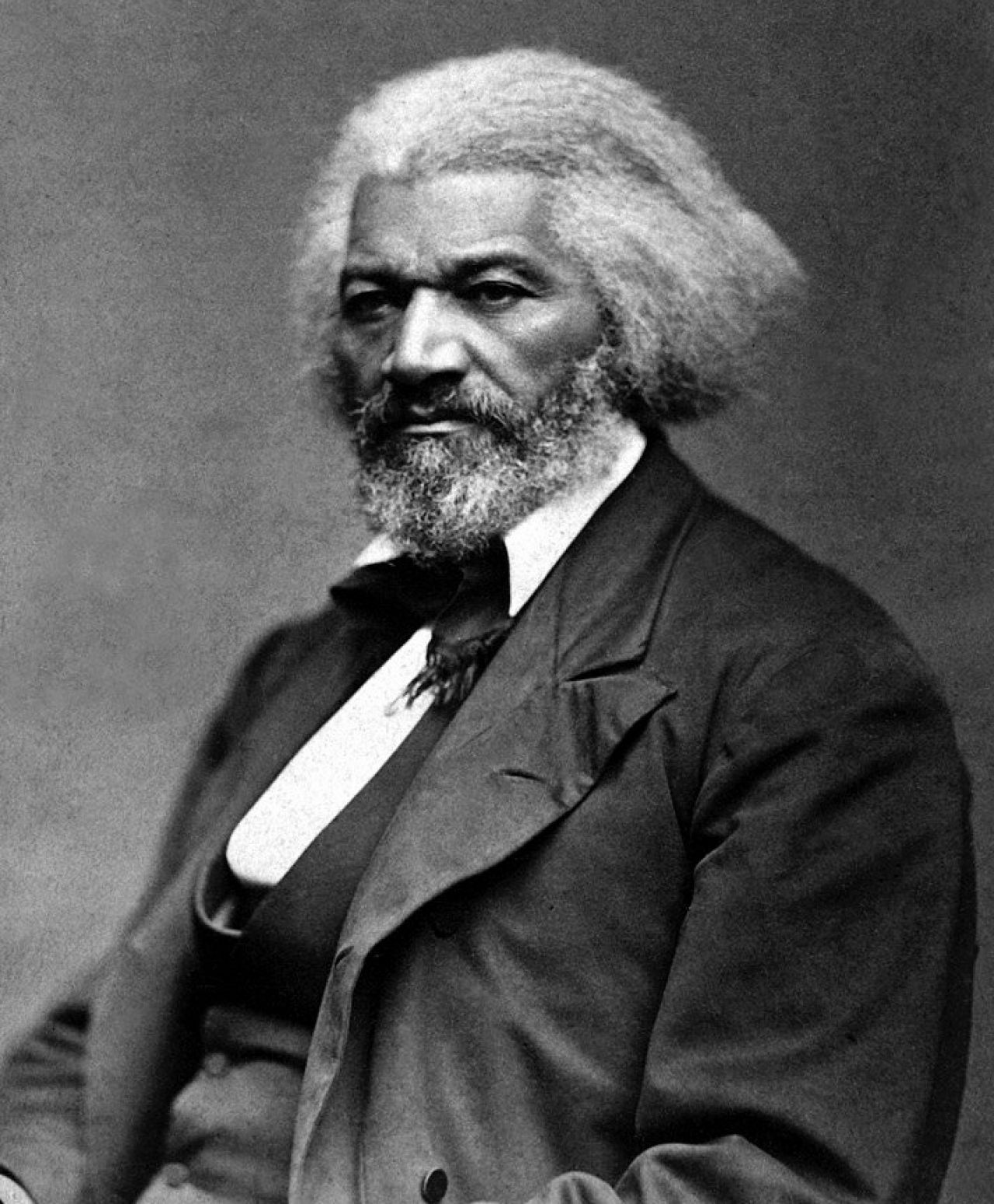 A man of color with a full head of hair and beard looks solemnly off the frame into the distance.