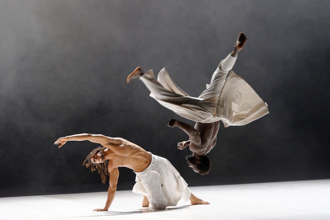 Two dancers dressed in flowing garb use each other to perform extreme kinetic movements.