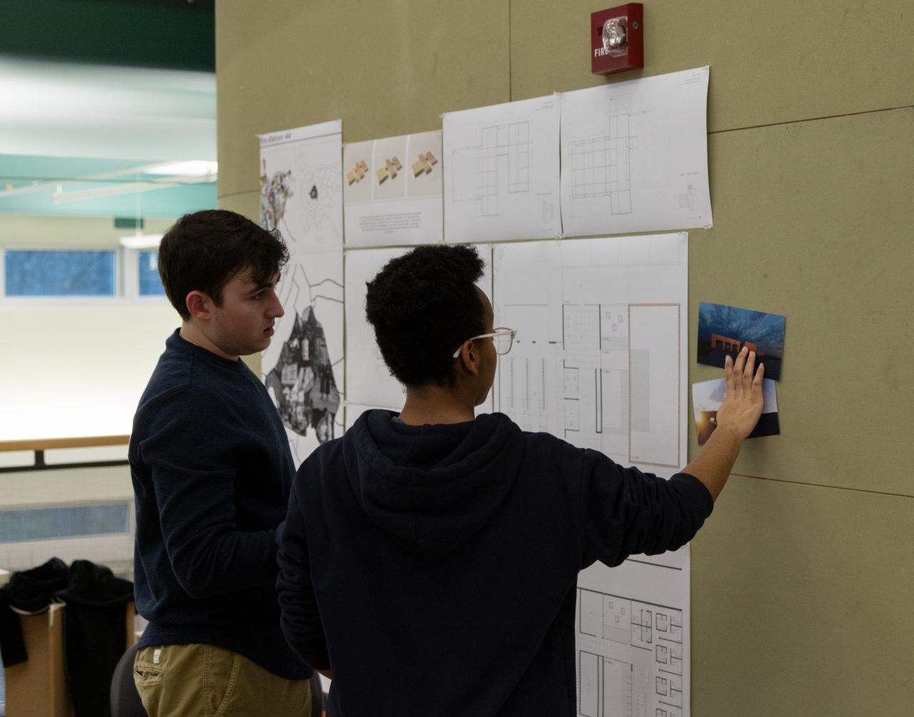 Two students looking at designs tacked to a wall