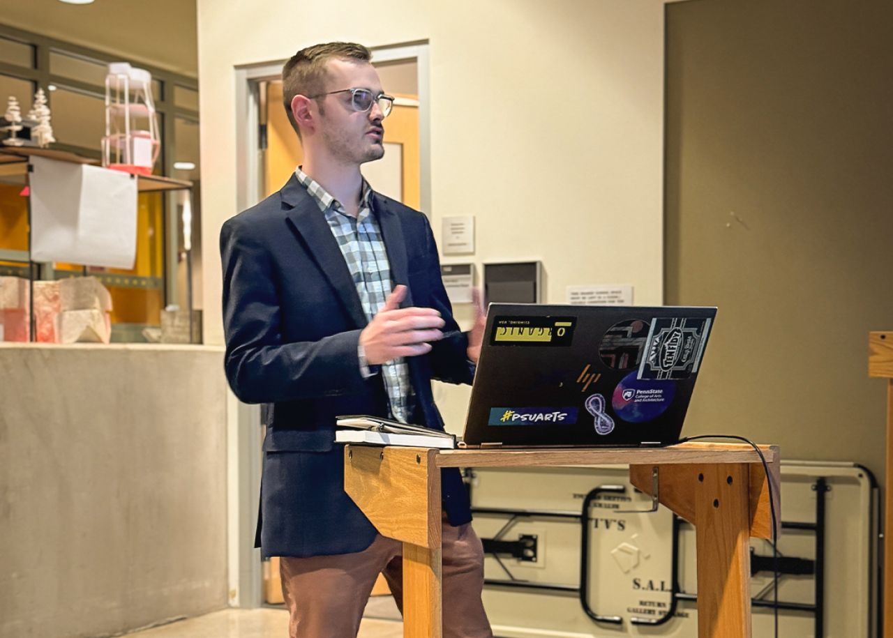 Kieron Cook stands at a podium with an open laptop in front of him.