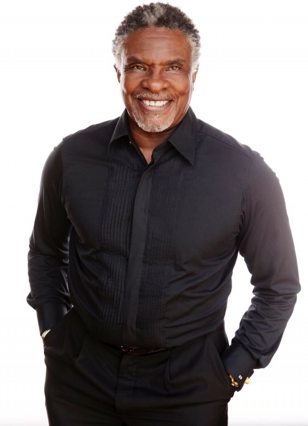 A man of color stands with his hands in his pockets and smiles.