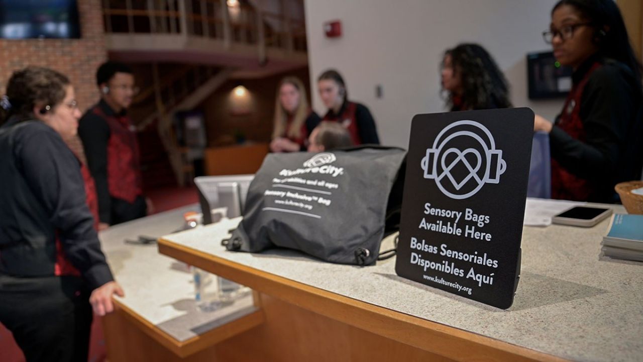 A sign and vinyl swag bag sit on top of a counter while a group of volunteers stand in the background.