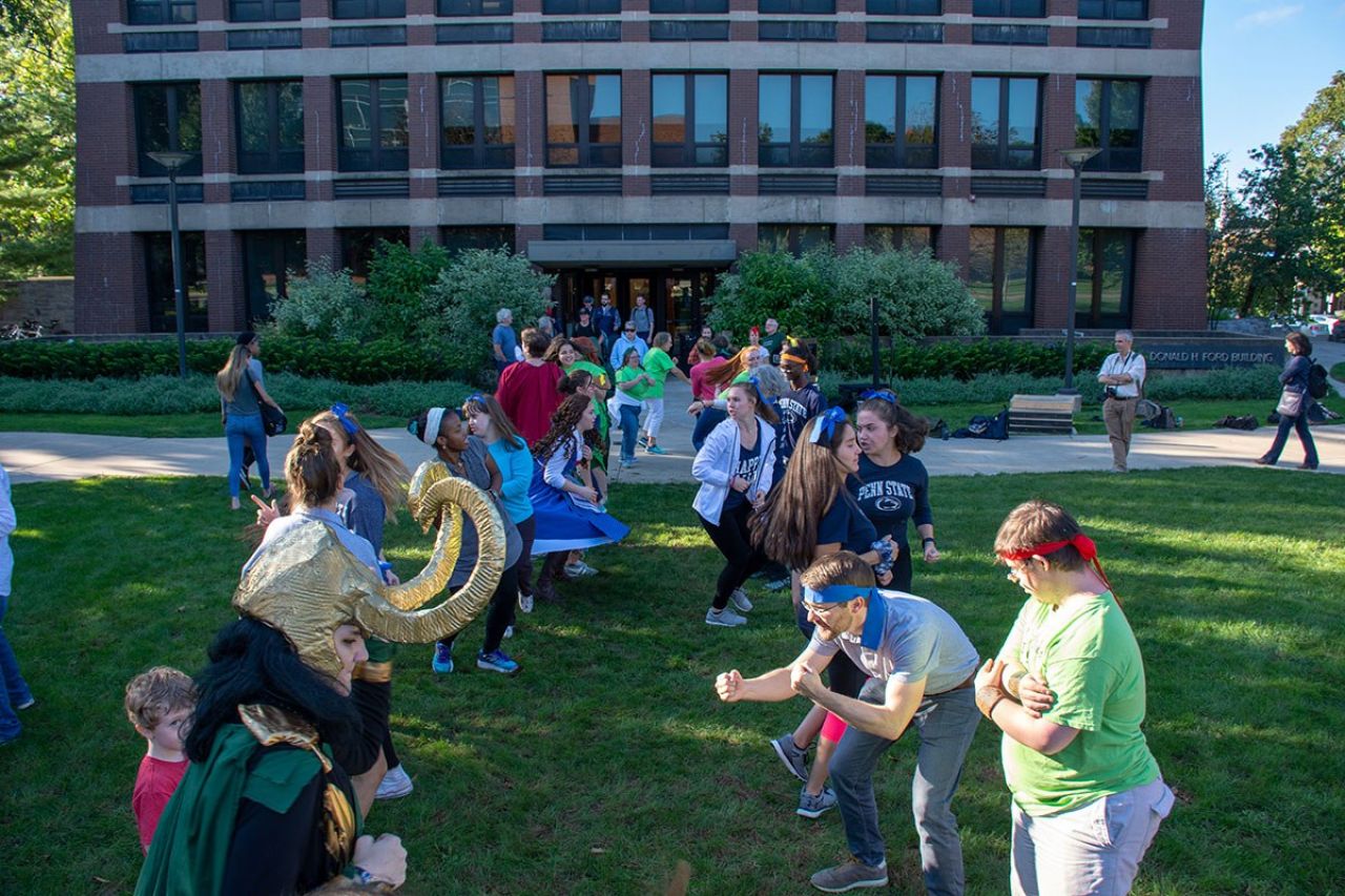 A group of people of all ages stand facing in two rows and dance without abandon.