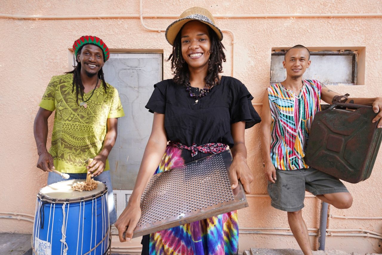 Three musicians hold their instruments made from beach trash.