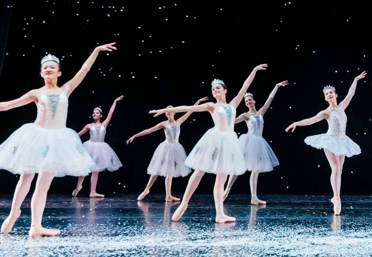 Young ballet dancers wearing matching tutus and tiaras strike a pose in unison.