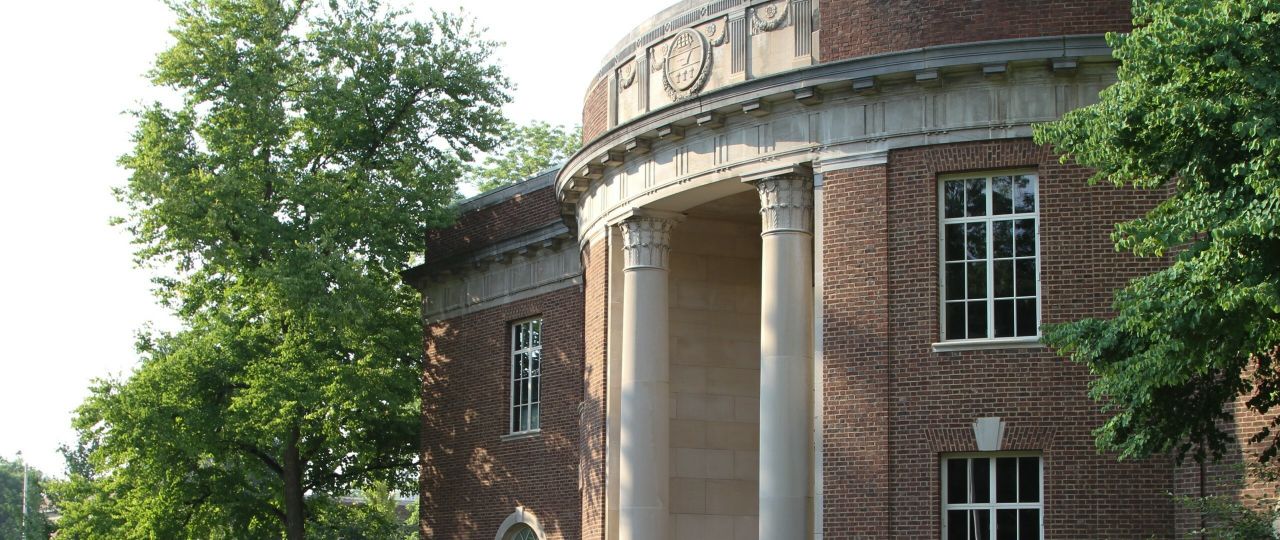 Brick and stone facade and columns of east entrance to Borland Building, all framed by green leafy trees.