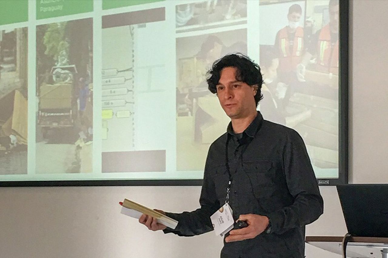 Julio Diarte stands to the right, motioning to a screen behind him which is displaying his research during a presentation.