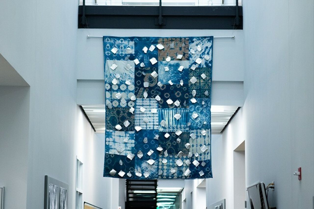 indigo-colored quilt hanging in a hallway of a campus building
