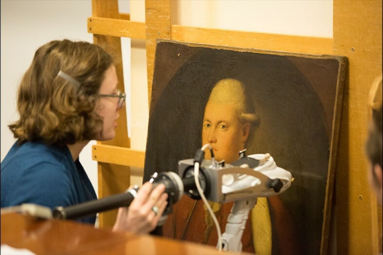 Profile shot of an art historian examining a portrait with an electronic scanning device.