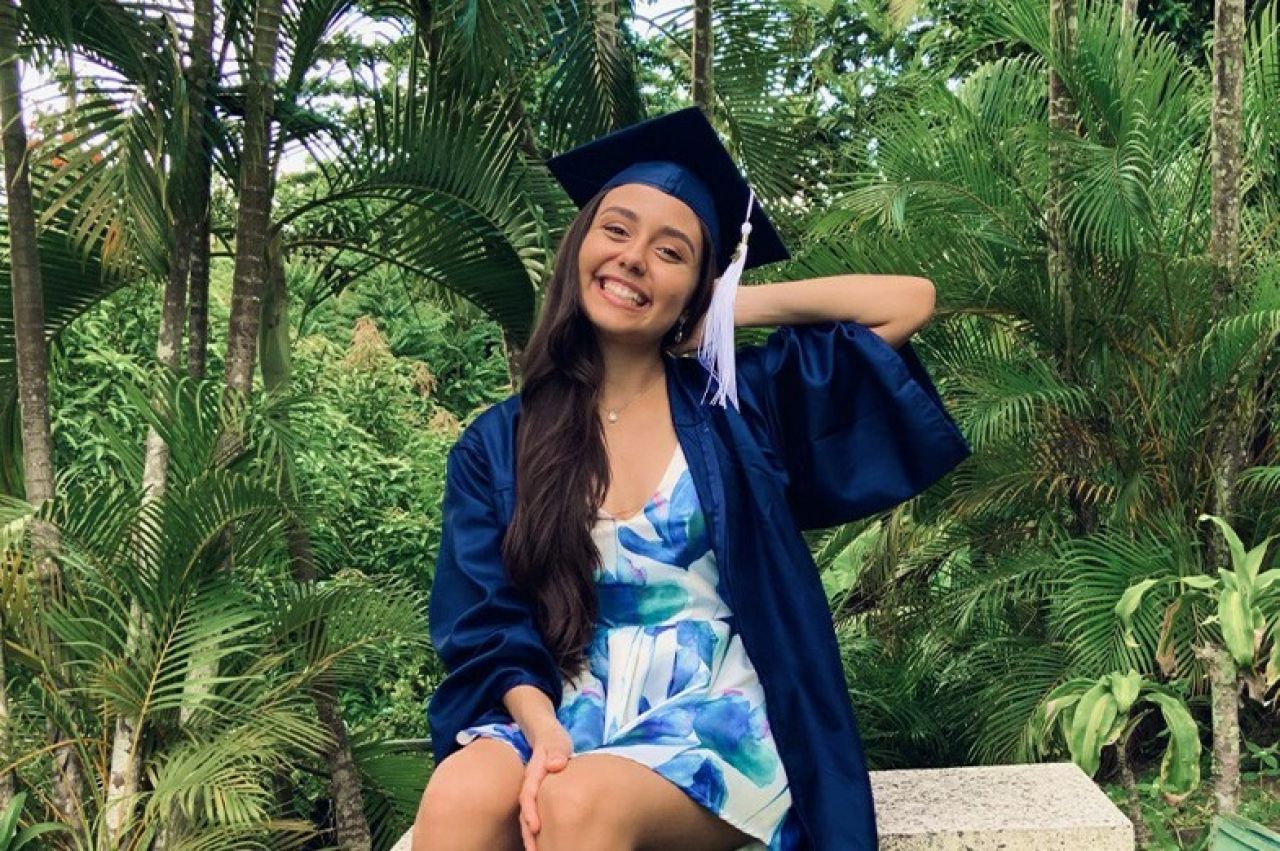 Female student marshal poses in front of tropical background