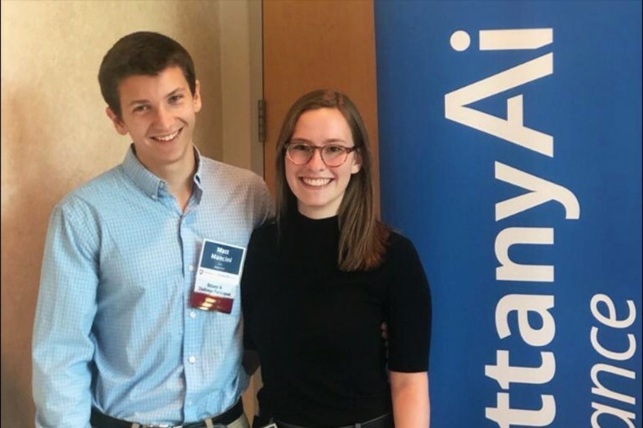 Matthew Mancini from the College of Engineering at left and Christie Warren pose next to the Nittany AI Challenge banner.