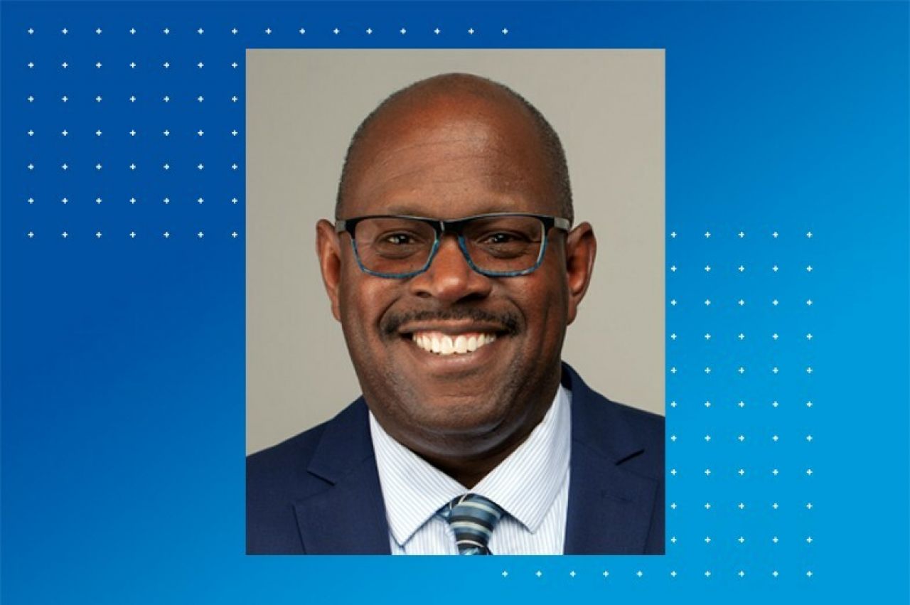 Head shot of a Black man with blue-framed glasses smiling.