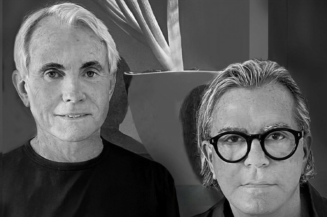 Black and white portrait of two men posing on front of a floral painting
